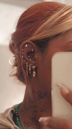 a close up of a person with tattoos on her face and behind their ear, holding a cell phone