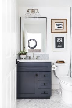 a white toilet sitting next to a bathroom sink under a mirror and framed pictures on the wall