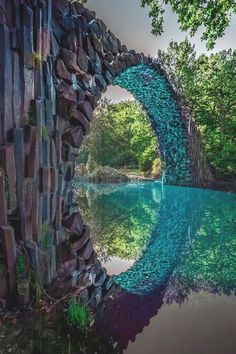 a stone bridge over a body of water surrounded by trees and rocks in the background