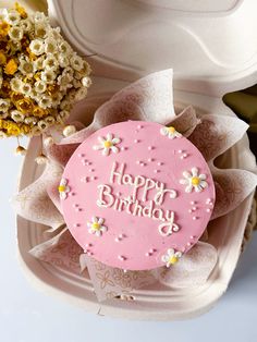 a pink birthday cake sitting on top of a white box next to flowers and popcorn