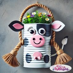 a tin can with a cow face and flowers in it, hanging from a rope