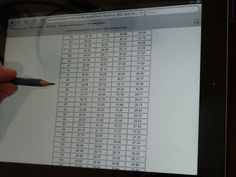 a person is holding a pencil in front of a computer screen with numbers on it