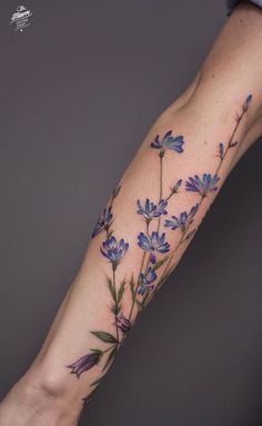 a woman's arm with blue flowers and leaves on the left side of her arm