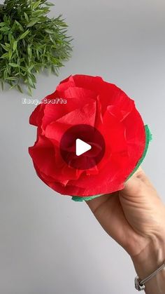 a hand holding a paper flower with a video playing button on it's center