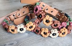 several bracelets with flowers on them sitting on a wooden table next to a leather belt