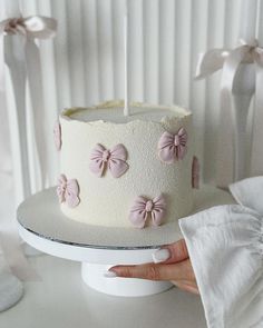 a white cake with pink bows on it and a person holding the knife in front of it