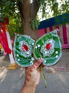 a hand holding a green and white plate with designs on it's face in front of a tree