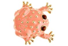 a pink and gold frog brooch sitting on top of a white surface with lots of dots