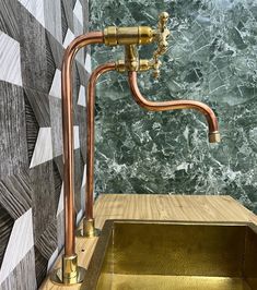 a gold sink in front of a green marble wall with copper faucets on it