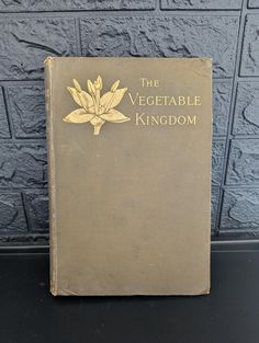 the vegetable kingdom book is sitting on a black table next to a gray brick wall