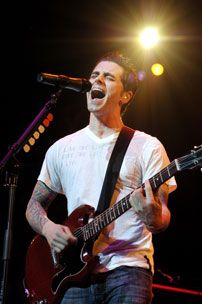 a man singing into a microphone while holding a guitar in front of him on stage