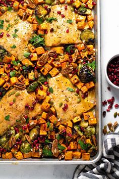 a sheet pan filled with sweet potato and brussel sprouts next to a bowl of pomegranates