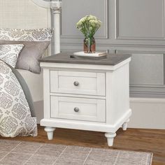 a white nightstand with two drawers on top of it next to a gray and white bed