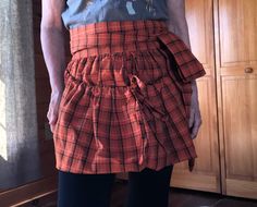 a woman standing in front of a wooden cabinet wearing an orange and black checkered apron