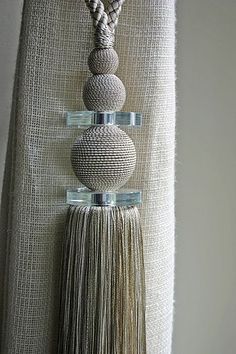 a wall hanging with three balls and tassels on it's sides in front of a curtain