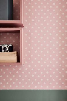 a pink shelf with a camera and some books on it next to a wallpaper