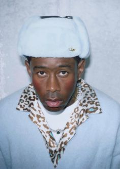 a man with a hat on his head and leopard print scarf around his neck is looking at the camera