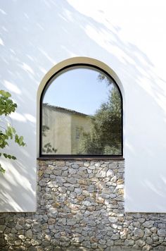 an arched window on the side of a white building with stone wall and bench in front