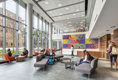 people are sitting in the lobby of an office building with large windows and artwork on the wall