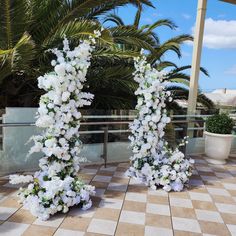 two tall white flowers are sitting on the ground next to each other in front of some palm trees