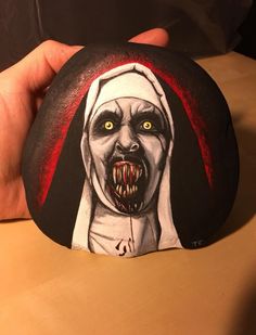 a hand painted rock with an evil nun on it's face and hands holding the rock