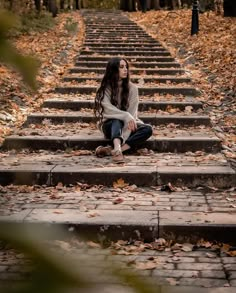 a young woman sitting on steps in the middle of an autumn forest with leaves all around her