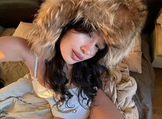 a woman laying on top of a bed wearing a furry hat