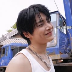 a young man standing in front of a blue truck with his eyes closed and wearing a chain around his neck