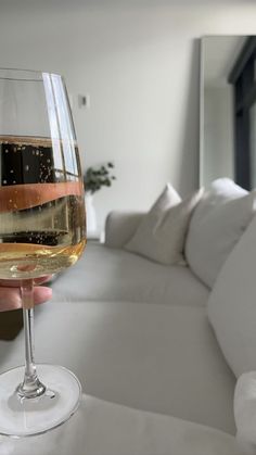 a person holding a glass of wine in front of a couch with pillows on it