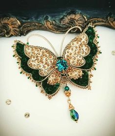 a green and gold butterfly brooch sitting on top of a table