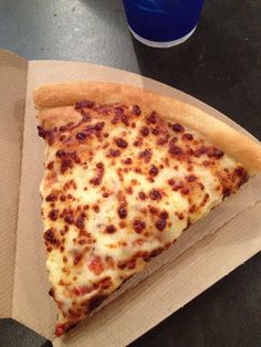 a slice of cheese pizza sitting on top of a cardboard box next to a drink