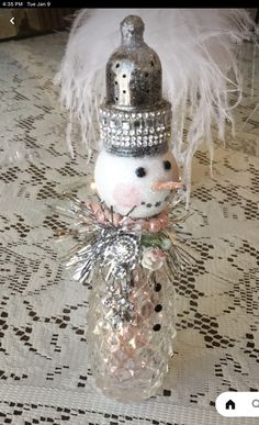 a snowman in a silver hat is sitting on a table with white and pink decorations