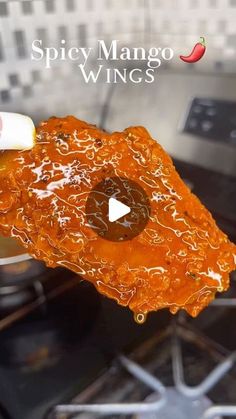 a close up of a piece of food on a stove top with the words spicy mango wings above it