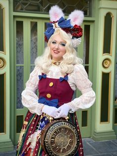 a woman dressed in an elaborate outfit with rabbit ears on her head and holding a clock