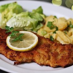 a white plate topped with fish, potatoes and lettuce next to a lemon wedge