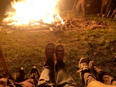 two people sitting in front of a campfire with their feet up on the ground