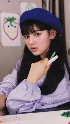 a young woman sitting at a table with two pens in her hand and an eraser next to her