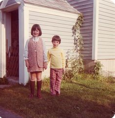 two young children standing in front of a house