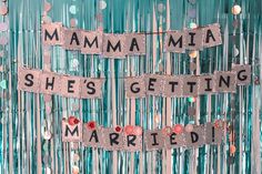 the words mamma she's getting married are spelled in silver letters on a blue backdrop