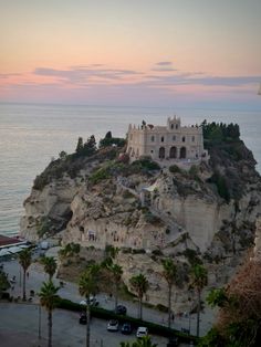 a castle on top of a cliff next to the ocean at sunset with palm trees