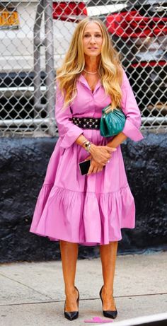 a woman in a pink dress is standing on the sidewalk with her hands in her pockets