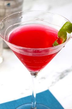 a red drink in a martini glass with a green garnish on the rim