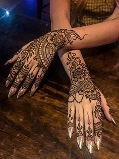 a woman's hands with henna tattoos on them sitting at a wooden table