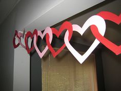 some paper hearts that are hanging on the side of a wall in front of a window