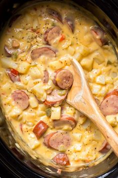 a wooden spoon in a slow cooker filled with macaroni, cheese and sausage