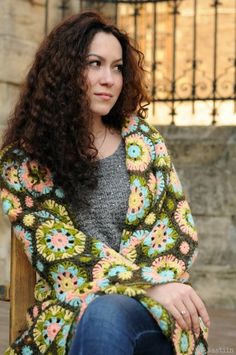 a woman with curly hair sitting on a bench wearing a crocheted shawl