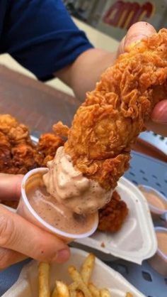 a person is eating some fried food from a container and dipping sauce on the chicken