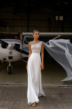 a woman standing in front of an airplane wearing a wedding dress with beading on it