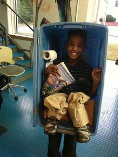 a young boy sitting in a blue box holding a roll of toilet paper and smiling