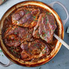 some meat is cooking in a skillet on a table with a wooden spatula